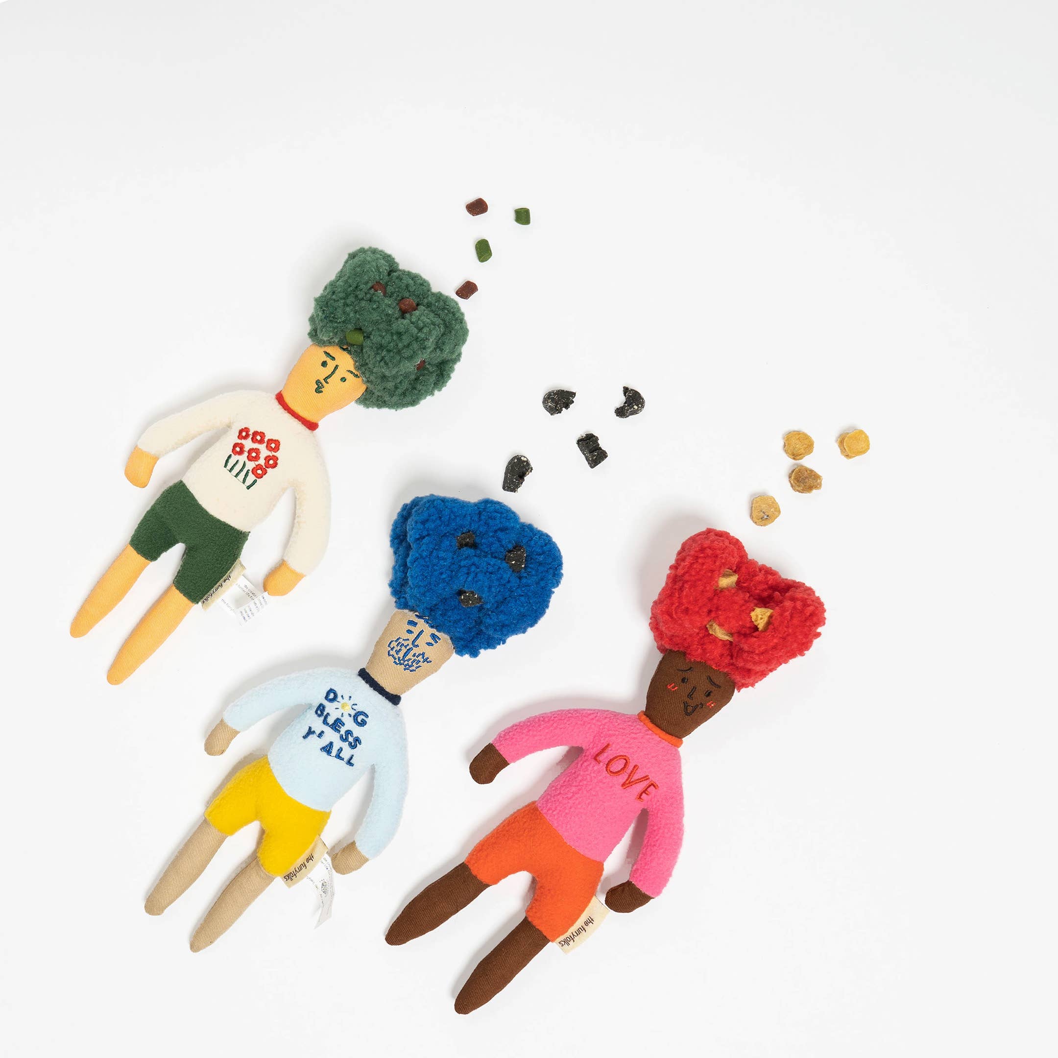 Three whimsical dolls with colorful, textured hair and playful outfits, surrounded by small colorful treats on a white background.
