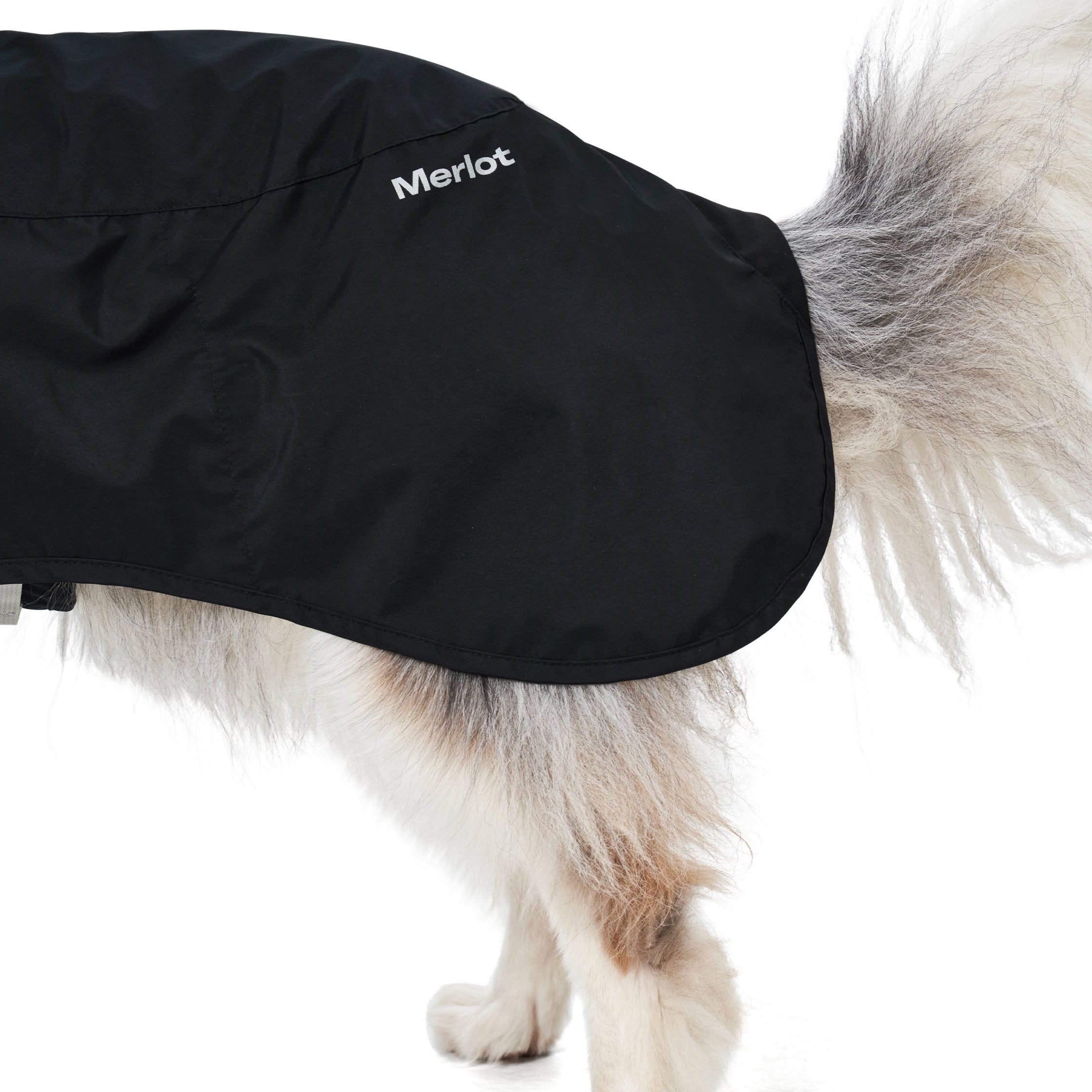 the rear of a white dog with a fluffy tail wearing a black raincoat with the brand name merlot