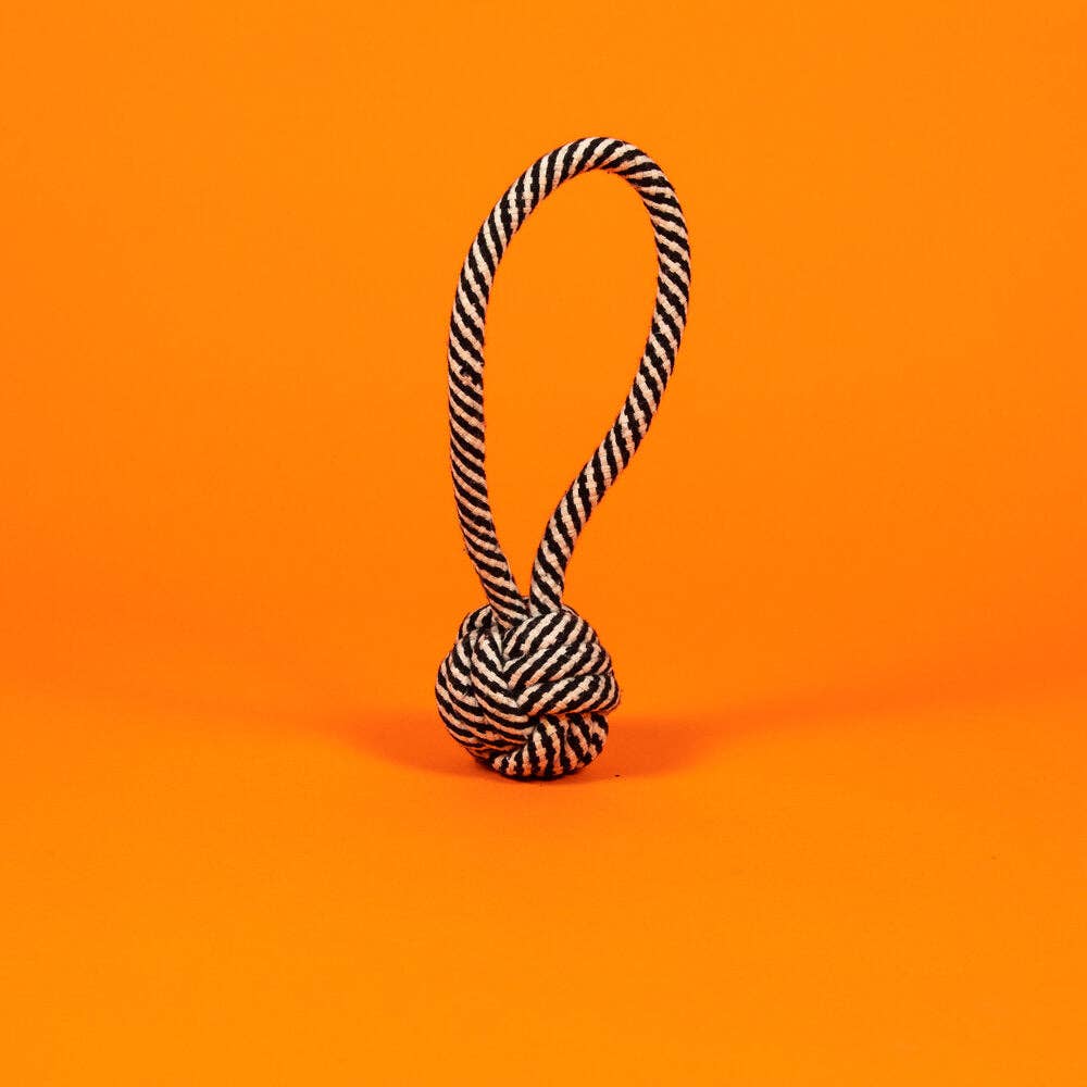 Black & white rope knot toy with loop handle, for dogs to chew and chase, set against an orange background.