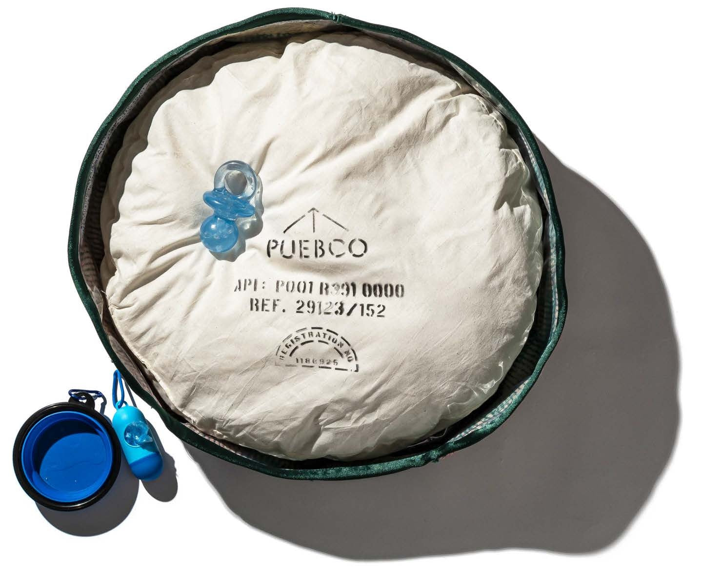 Puebco dog bed with blue dog toy and bowl on a white background