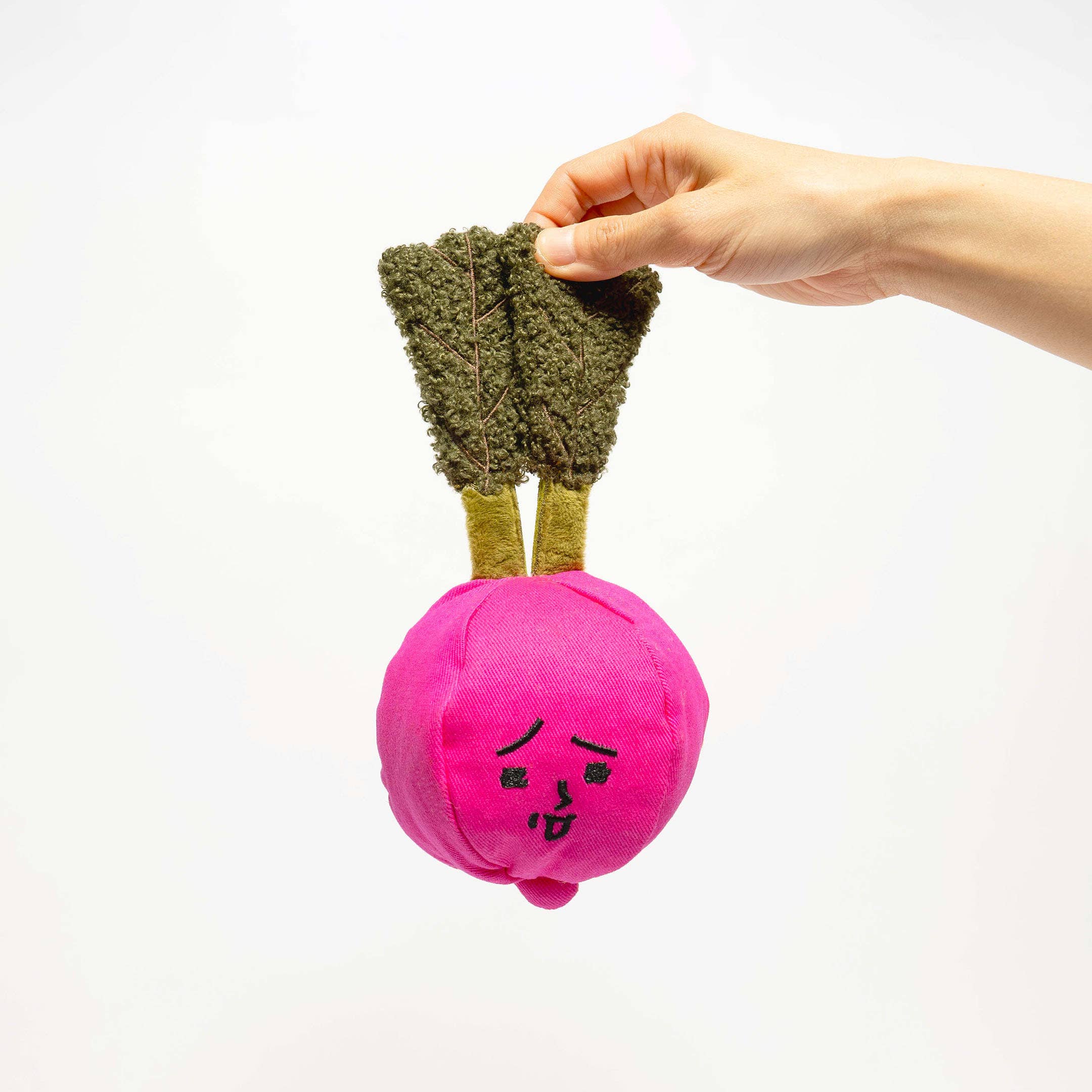 Hand holding a pink vegetable-shaped toy with green leaves on a white background
