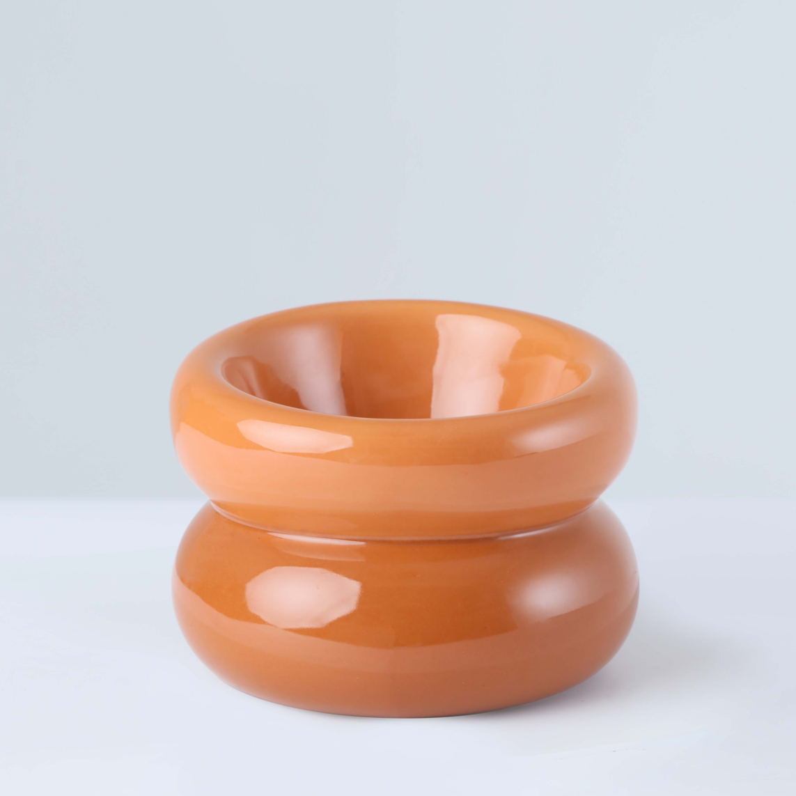 A smooth, glossy terracotta-colored ceramic bowl with a rounded, stacked design against a light background.