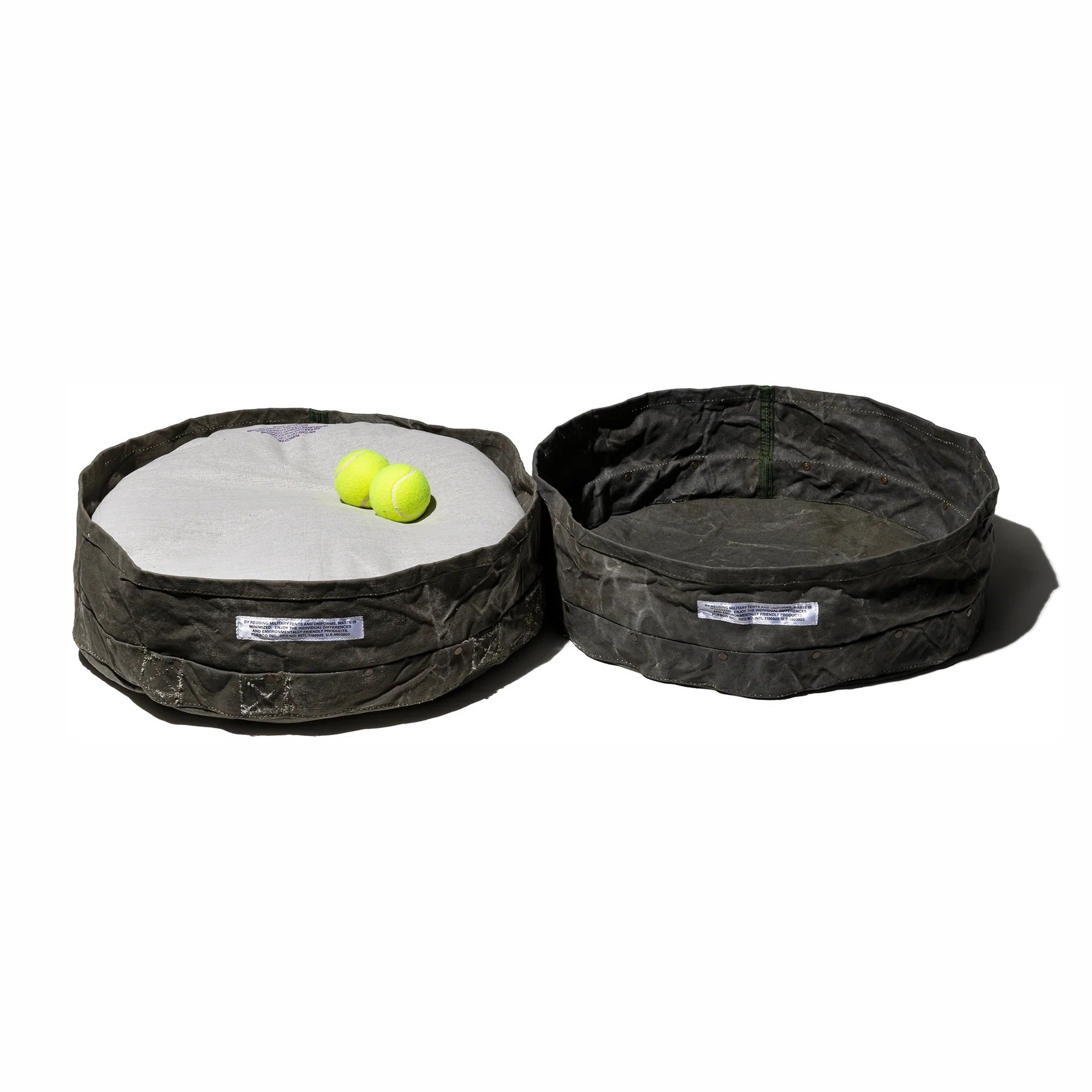 Two black pet beds with a white cushion and two yellow balls on a white background