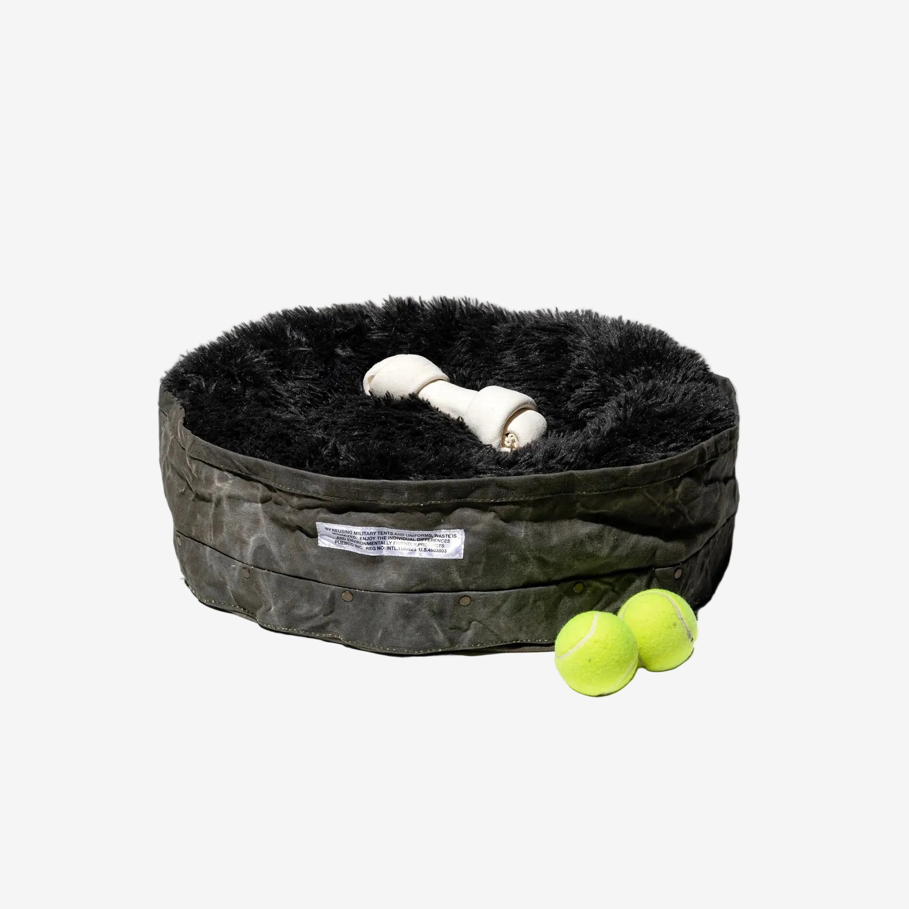 Pet bed with a plush black interior, a bone-shaped toy, and two green tennis balls on a white background.