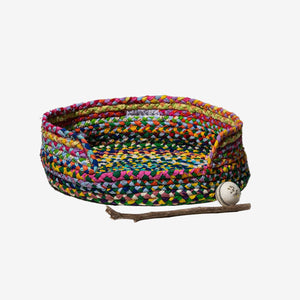 Colorful braided pet bed with a ball and stick on a white background