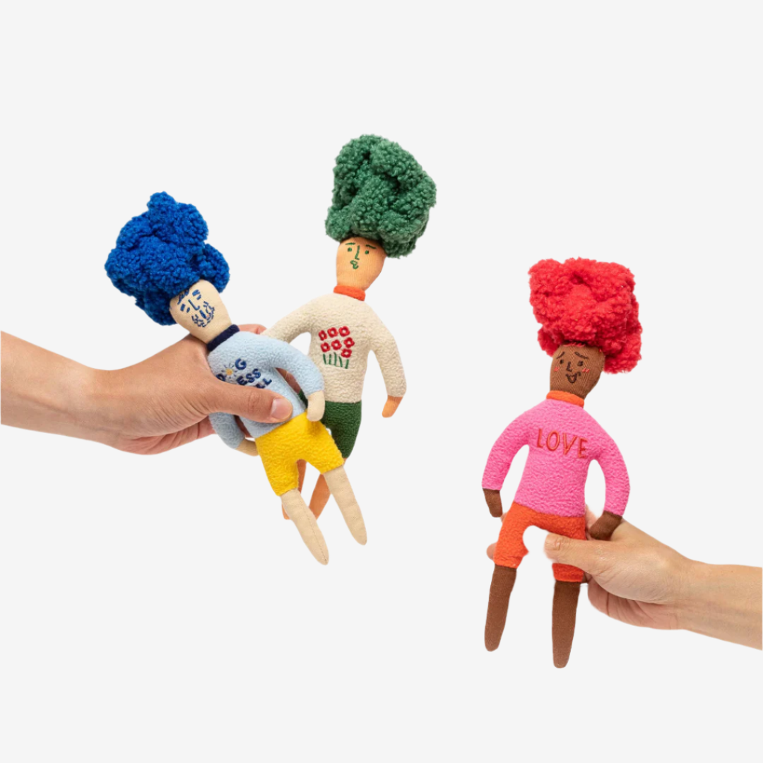 Three whimsical dolls with colorful, textured hair and playful outfits, surrounded by small colorful treats on a white background.