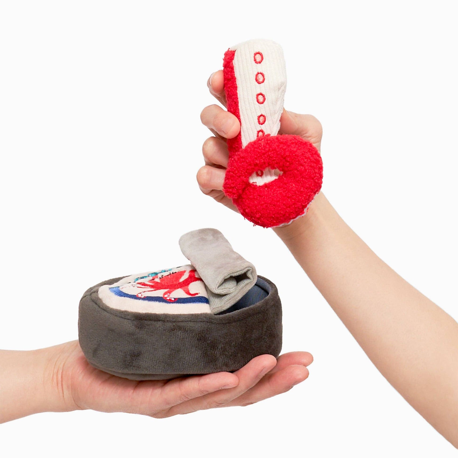 A hand holds a plush dog toy octopus leg, above another hand holding the toy tin for it to go in. 