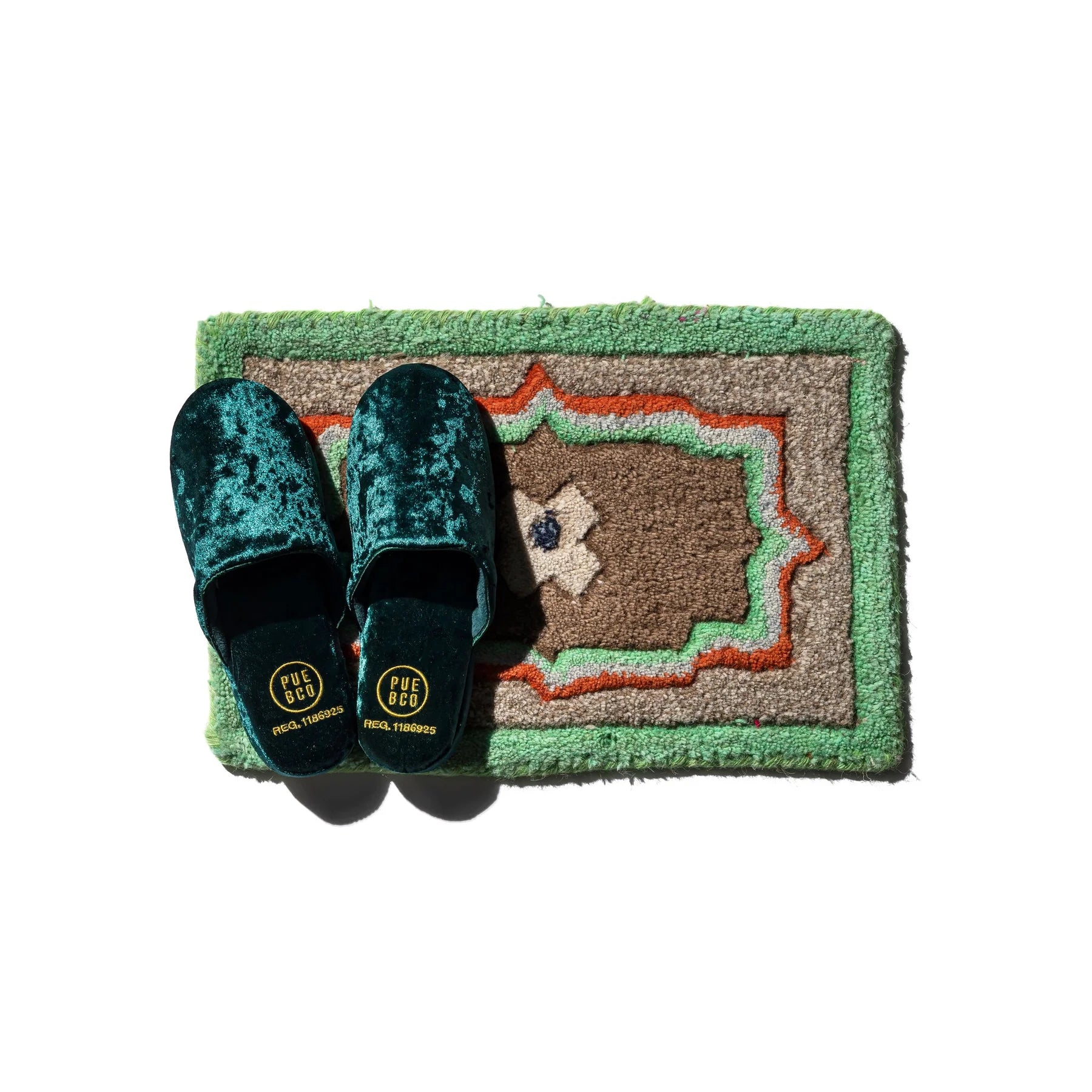 Pair of green velvet slippers on a decorative rug with a white background